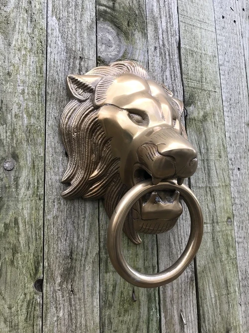 A lion's head, made of aluminum in a brass color, as a door knocker